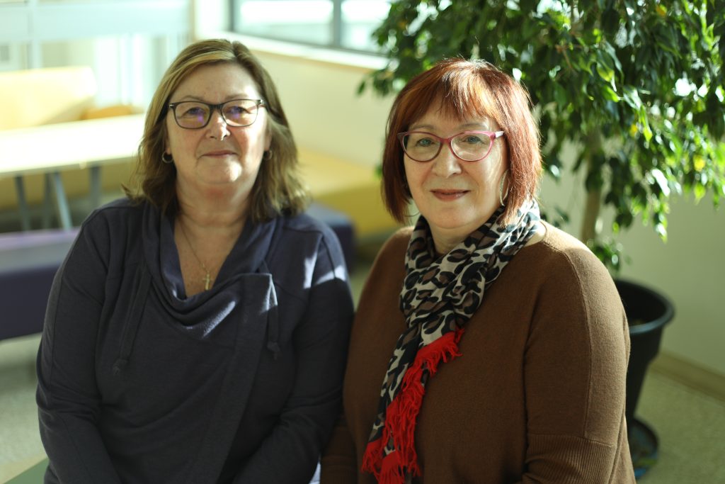 deux dames sourient ensemble avec un arbre vert en arrière-plan